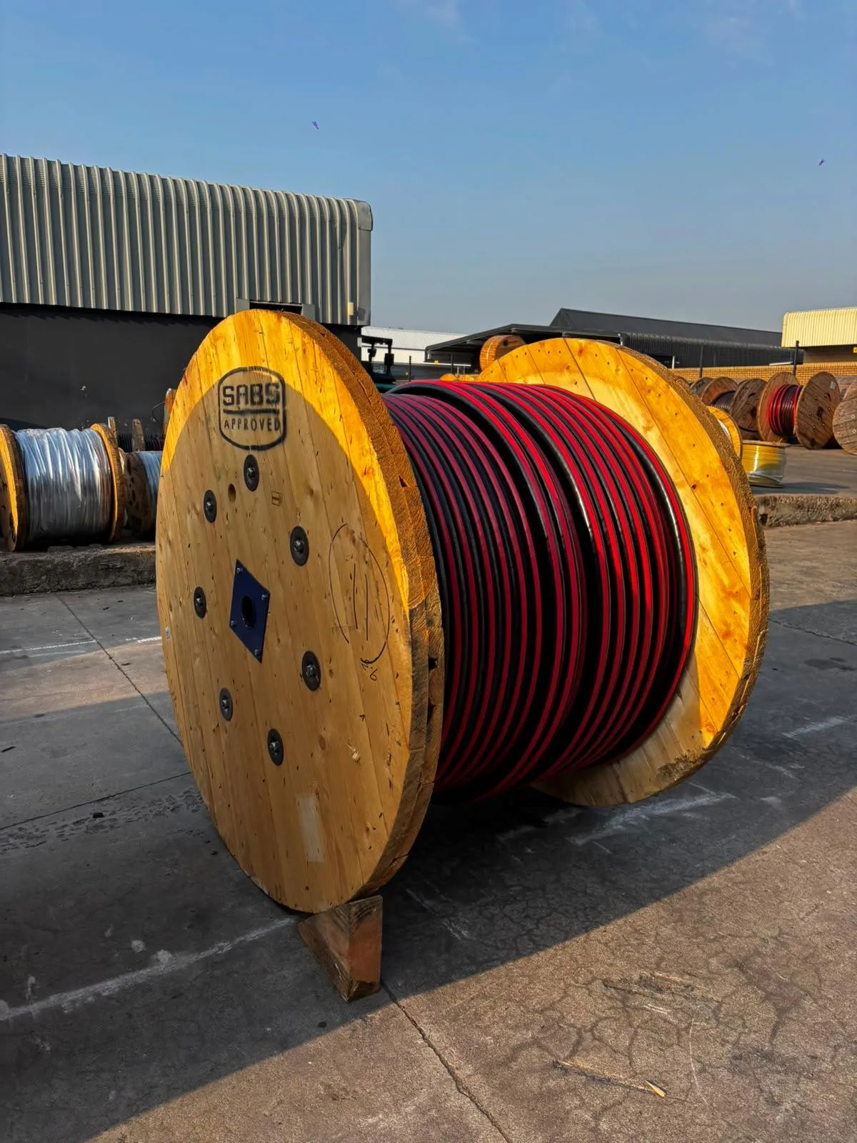 Red and black cable supplied on a wooden drum in a supplier yard.